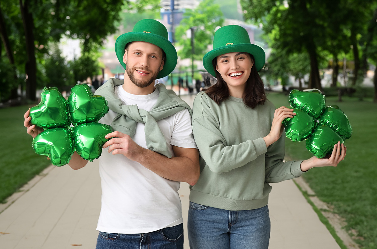 Two people with green hats holding shamrock balloons