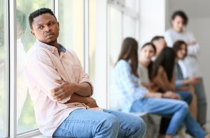 Male isolated looking lonely with a group of people in the distance.